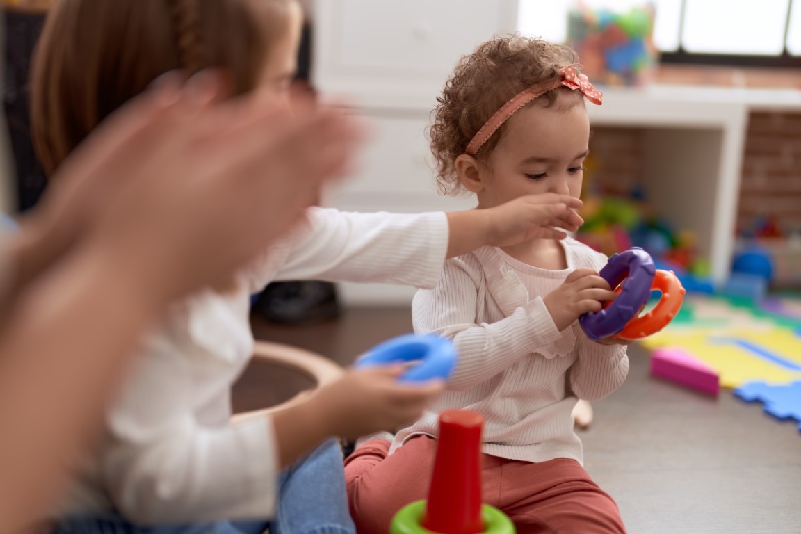 Adorable caucasian girl playing with hoops sitting on floor at kindergarten